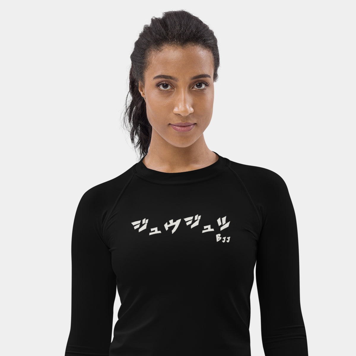 Woman wearing the Women’s BJJ KATAKANA Long-Sleeve Rash Guard in Iron Black, front view showing the off-white katakana and BJJ chest print
