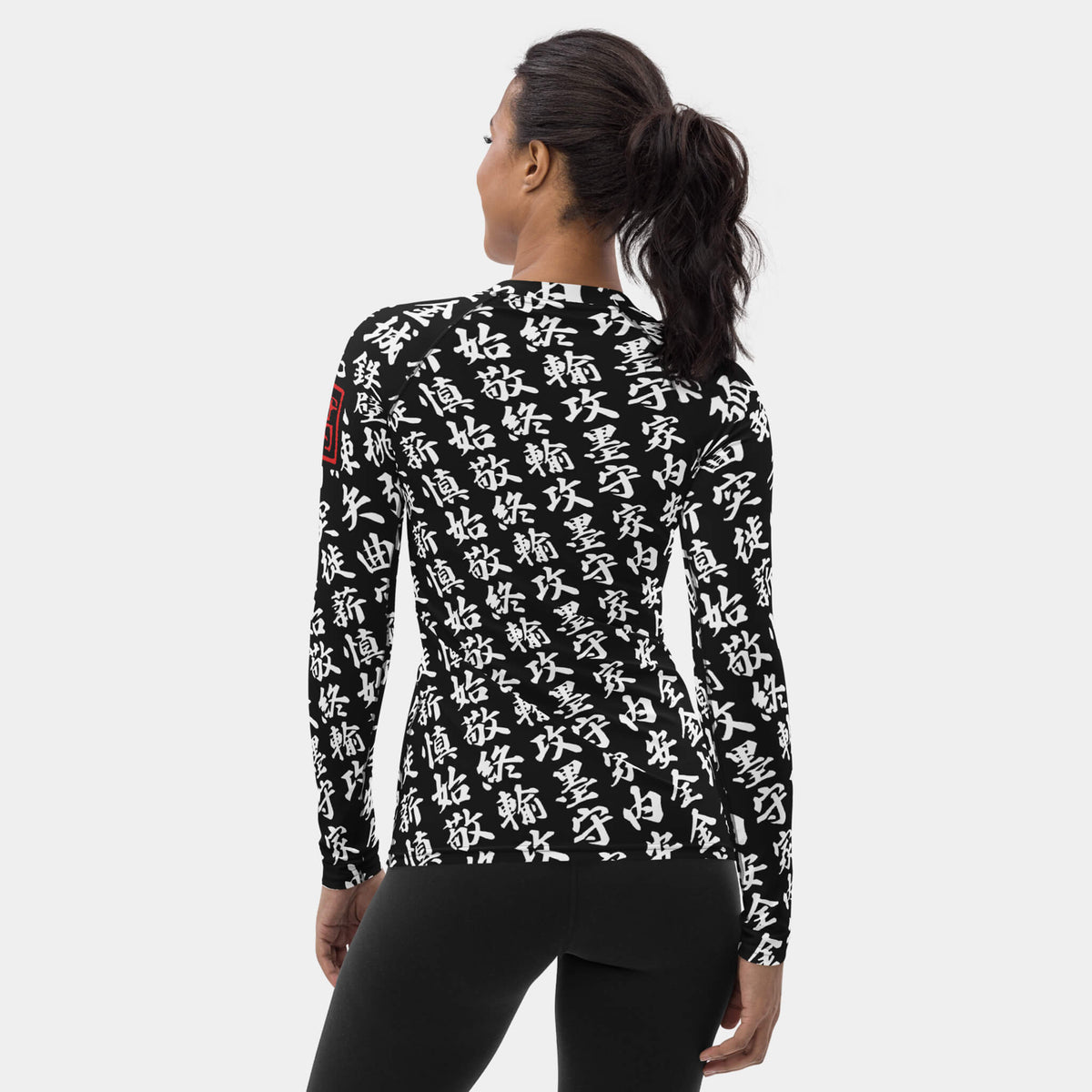 Back view of the women's TOO MUCH KANJI long-sleeve BJJ rash guard in Iron Black and White, showing the all-over white kanji print